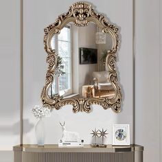 an ornate gold framed mirror on a wall above a console table with a white vase