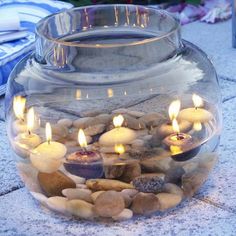 a glass bowl filled with rocks and candles on top of a stone floor next to flowers