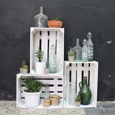 three wooden crates with plants and bottles on them sitting next to each other in front of a black wall