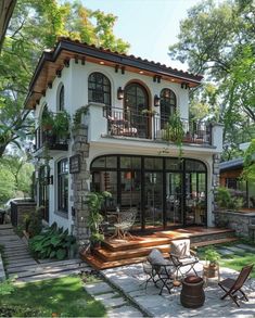 a large white house with lots of windows and plants on the front porch, surrounded by greenery