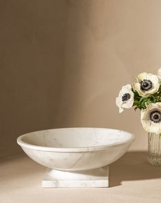 a marble bowl and vase with white flowers in it on a beige surface next to a wall