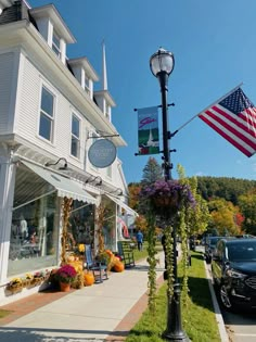 an american flag flying in front of a store on a street with cars parked nearby