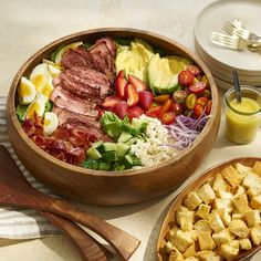 a wooden bowl filled with meat and veggies next to two bowls of salad