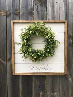 a welcome sign with a wreath hanging on the side of a wooden fence behind it