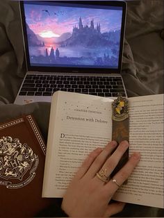 a person is reading a book in front of a laptop computer with the hogwarts logo on it