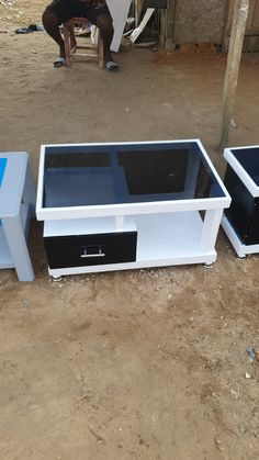 three white and black tables sitting on dirt ground next to a person in the background