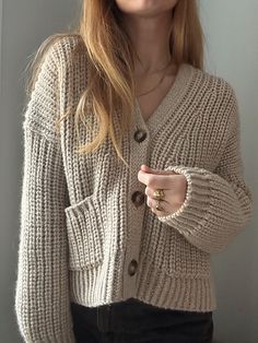 a woman wearing a white cardigan sweater and black pants is posing for the camera