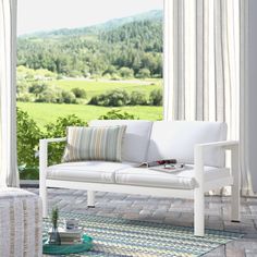 a white couch sitting on top of a wooden floor next to a large window covered in curtains