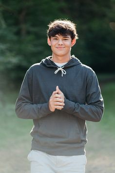 a young man standing in front of a field with his hands crossed and smiling at the camera