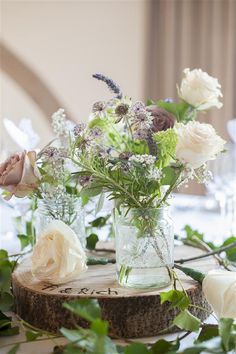 flowers in vases sitting on a table with greenery and wine glasses behind them