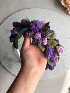 a hand holding a purple flower on top of a white plate