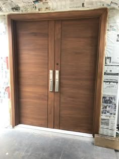 two large wooden doors with newspaper coverings on the wall behind them in an empty room