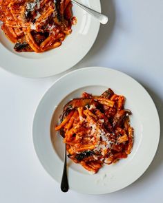 two white plates topped with pasta covered in sauce