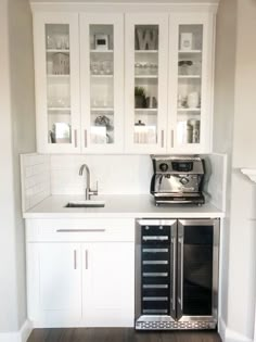 an empty kitchen with white cabinets and wood flooring in the center is seen from across the room