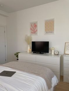 a white bedroom with a flat screen tv on top of the dresser and two vases next to it