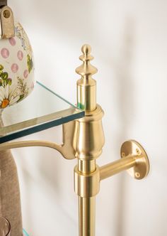 a gold faucet on a glass shelf next to a vase