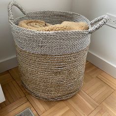 a large woven basket sitting on top of a hard wood floor next to a white wall