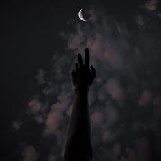 a hand reaching up into the sky at night with clouds and a half moon in the background