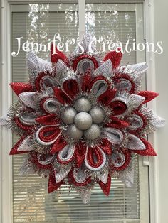 a red and silver christmas wreath on a window sill with the words jeanette's creations above it