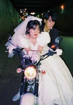 a bride and groom are riding on a motorcycle together in an alleyway at night