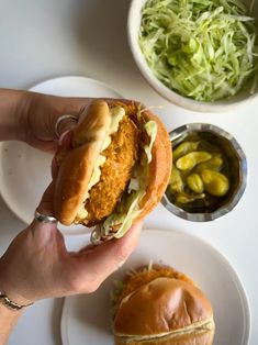 a person is holding up a chicken sandwich on a plate with coleslaw and pickles