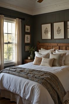 a bed with white sheets and pillows in a bedroom next to two windows, framed pictures on the wall