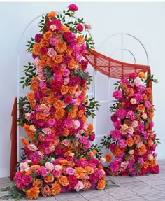 an arrangement of flowers on display in front of a white wall with orange and pink accents