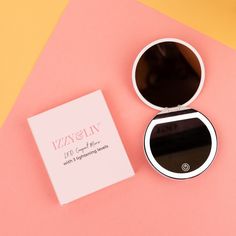 an open compact mirror next to a white box on a pink and yellow tablecloth