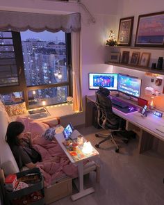 a person sitting on a couch in front of a desk with two monitors and a laptop