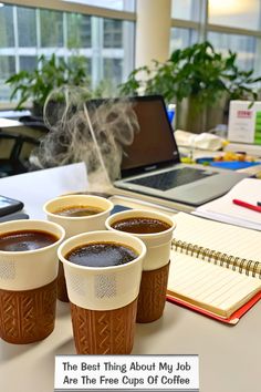 four cups of coffee sitting on top of a desk next to a notebook and laptop