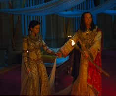 two people dressed in costume holding hands and standing next to each other with lights on