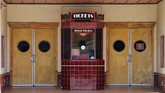 an empty building with three doors and two windows on each side, in front of the door is a ticket machine