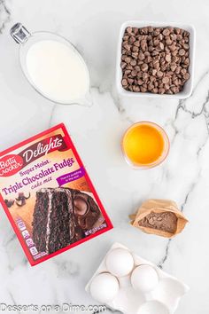 ingredients to make chocolate fudge cake laid out on a white marble counter with milk and eggs