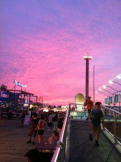 many people are walking up and down the stairs at an amusement park as the sun sets