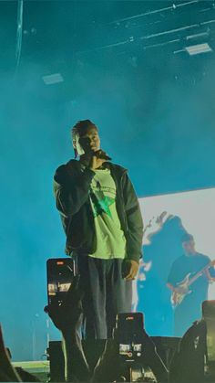 a man standing on top of a stage holding a cell phone to his ear while wearing a green shirt