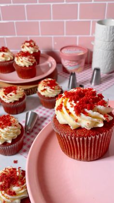 cupcakes with white frosting and red sprinkles on pink plates