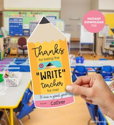 a hand holding up a teacher appreciation card in front of a classroom full of desks