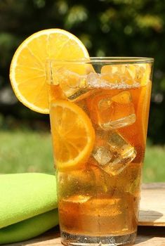 a glass filled with ice and lemon slices on top of a wooden table next to a green towel