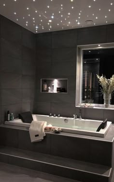 a bath tub sitting under a window next to a vase with white flowers in it