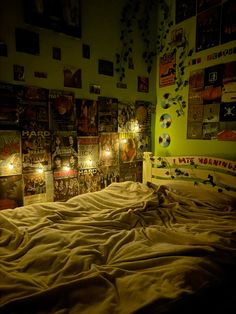 an unmade bed with posters on the wall and lights in the room above it