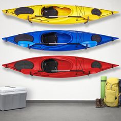 three kayaks lined up against a white wall with storage bins on the floor