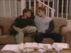 two young men sitting on a couch in front of an open book and paper bags