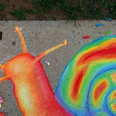 a colorful snail drawn on the sidewalk next to some crayons and colored pencils