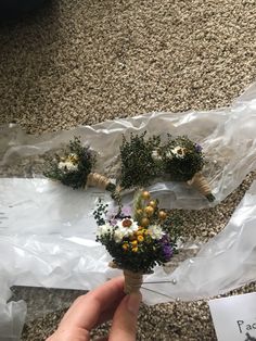 someone is holding some flowers in their hand on the ground next to plastic wrap and paper