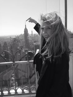 a woman standing on top of a building with her hand in the air and looking at the camera