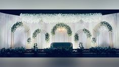 a stage set up for a wedding with flowers and greenery on the side wall