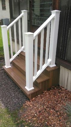 a wooden deck with white railing and handrails in front of a home door