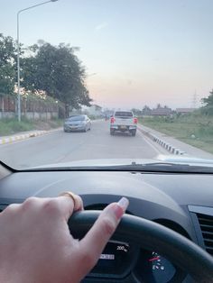 a hand on the steering wheel of a car driving down a road with other cars