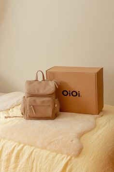 a small backpack sitting on top of a bed next to a brown box and pillow