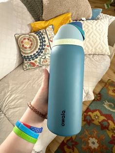 a person holding a blue water bottle in their hand on top of a bed with pillows